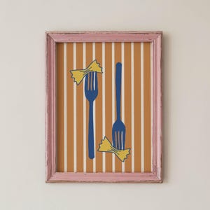 Pode incluir: Uma impressão de arte emoldurada com um fundo amarelo mostarda e riscas verticais brancas. Dois garfos azuis estão ilustrados no centro, cada um posicionado com uma massa amarela em forma de laço, tudo dentro de uma moldura rosa desgastada.