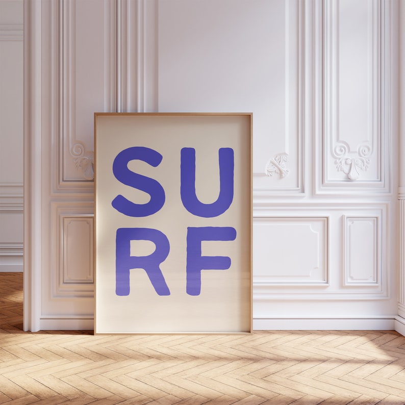 May include: A framed print with the word "SURF" in large, purple letters on a cream background.