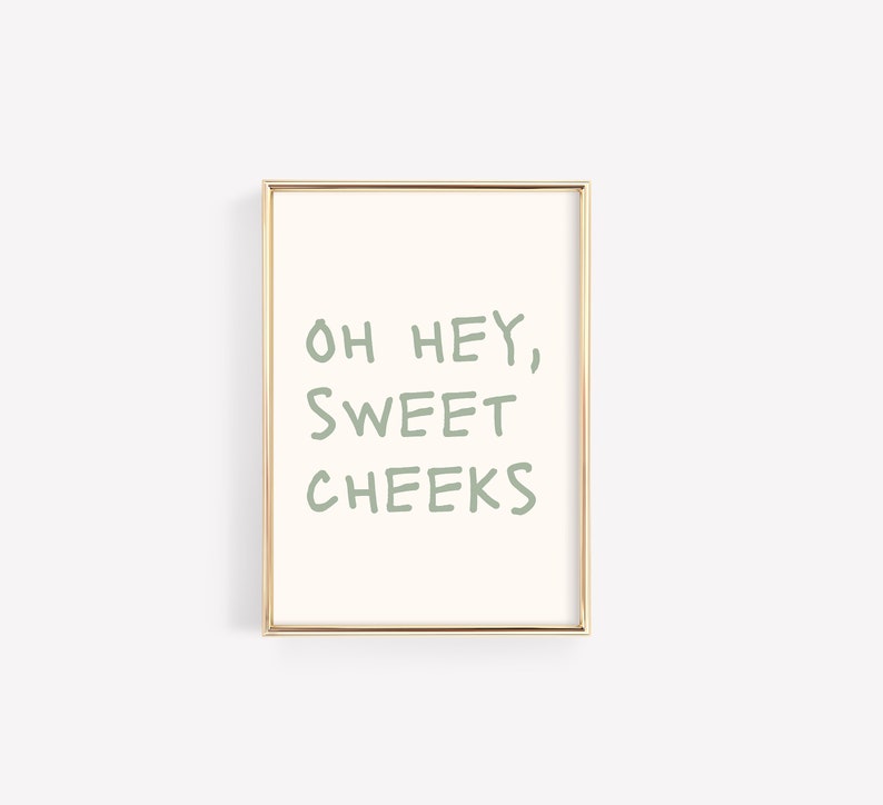 Może przedstawiać: Wydruk w ramie ze złotą ramką i białym tłem. Tekst "OH HEY, SWEET CHEEKS" jest napisany na zielono.