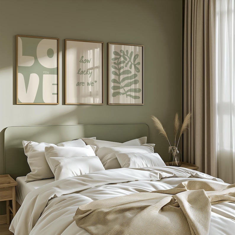 May include: Three framed prints on a sage green wall above a bed with white bedding. The prints feature a white graphic of the word "LOVE" with the word "YOU" in smaller letters, a green graphic with the text "how lucky are we", and a green abstract leaf design.