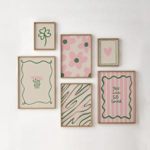May include: A collection of framed art prints with a gold border. The prints feature various designs, including a four-leaf clover, pink flowers, a heart, abstract lines, and the text "You are SO loved" on a pink striped background.