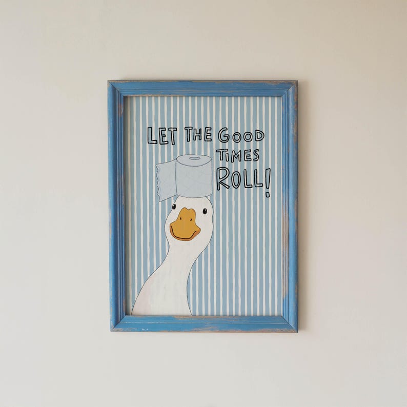 May include: A framed wall art print featuring a white goose with an orange beak balancing a roll of toilet paper on its head. The background has vertical light blue and white stripes. The text reads: LET THE GOOD TIMES ROLL!