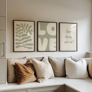 May include: Three framed prints in a green and white colour scheme. The left print features a stylised green leaf design. The centre print says "LOVE YOU" in white letters on a green background. The right print says "how lucky are we" in green letters on a white background.