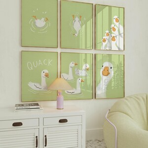 Puede incluir: Un conjunto de seis impresiones enmarcadas con ilustraciones de patos blancos sobre un fondo verde claro. Las impresiones est&aacute;n dispuestas en una cuadr&iacute;cula en una pared blanca. La fila superior presenta un pato buceando en el agua, un pato boca abajo y un grupo de patos mirando al espectador. La fila del medio presenta un pato nadando con el texto "QUACK" encima, un grupo de patos nadando y un pato nadando con la cabeza fuera del agua. La fila inferior presenta un pato nadando con la cabeza fuera del agua.