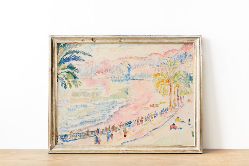 May include: A framed watercolor painting of a beach scene with palm trees, figures, and buildings. The artwork features pastel colors, including pink, blue, and yellow. The frame is a light, neutral color.