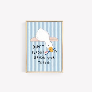 May include: A framed wall art print featuring a white duck with an orange beak holding a blue toothbrush with red toothpaste. The background has vertical light blue and white stripes. The text reads: DON'T FORGET TO BRUSH YOUR TEETH!