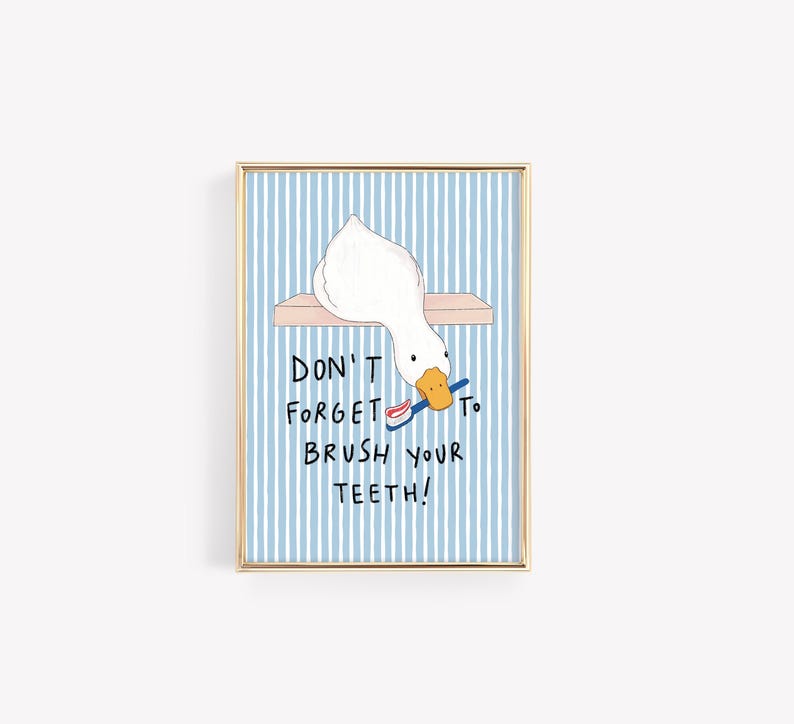 May include: A framed wall art print featuring a white duck with an orange beak holding a blue toothbrush with red toothpaste. The background has vertical light blue and white stripes. The text reads: DON'T FORGET TO BRUSH YOUR TEETH!