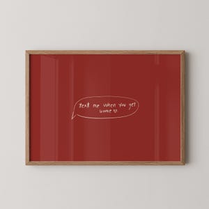 Puede incluir: Una impresión artística enmarcada con un fondo rojo liso. La impresión presenta un bocadillo blanco con el texto escrito a mano "text me when you get home ♡". El marco es de madera.