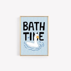 May include: A framed wall art print featuring a white goose with an orange beak swimming in blue water. The background consists of vertical light blue and white stripes. The black hand-drawn text BATH TIME is centered above the goose illustration.