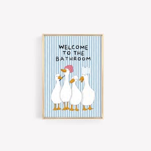 May include: A framed wall art print featuring a light blue and white vertical striped background with the text WELCOME TO THE BATHROOM. Four white ducks with orange beaks and feet are illustrated, one wearing a pink shower cap and one with toilet paper.