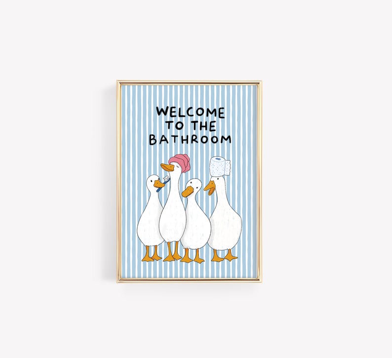 May include: A framed wall art print featuring a light blue and white vertical striped background with the text WELCOME TO THE BATHROOM. Four white ducks with orange beaks and feet are illustrated, one wearing a pink shower cap and one with toilet paper.