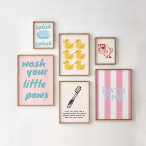 Può includere: Una collezione di stampe artistiche incorniciate a tema bagno. Le stampe presentano illustrazioni e testo giocosi, tra cui frasi come "splish splash", "wash your little paws" e "bath time". La tavolozza dei colori include rosa, blu e giallo.