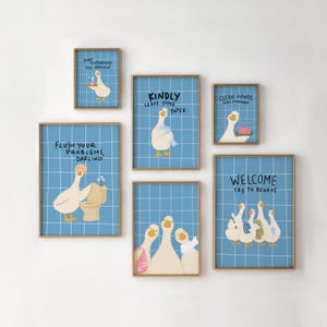 May include: A set of six framed wall art prints featuring cartoon geese on a blue grid background. The prints include text such as Your Toothbrush Has Arrived, Kindly Leave Some Paper, Clean Hands, Flush Your Problems, and Welcome Try To Behave.