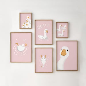 May include: A set of six framed art prints featuring illustrations of white geese on a pink background. The prints include images of geese swimming, a close-up of a goose face, and the word "QUACK". The frames have a gold finish.