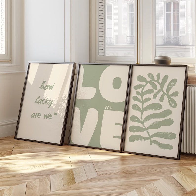 May include: Three framed prints with a minimalist design. The left print has the text "how lucky are we" in green script. The middle print has the word "LOVE" in large white letters on a green background. The right print has a green abstract design of leaves and branches.