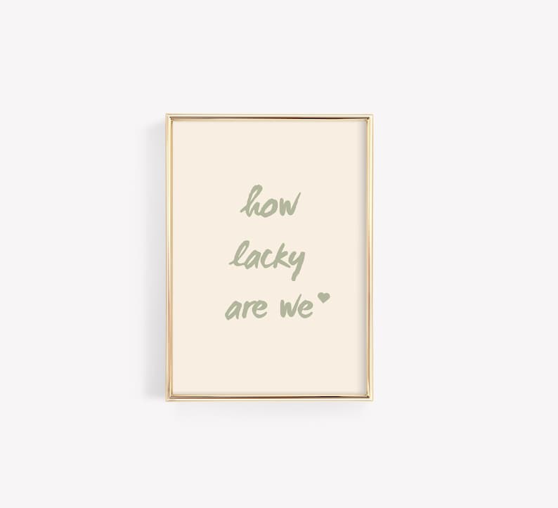 May include: A framed print with a light beige background and gold frame. The text "how lucky are we" is written in green.