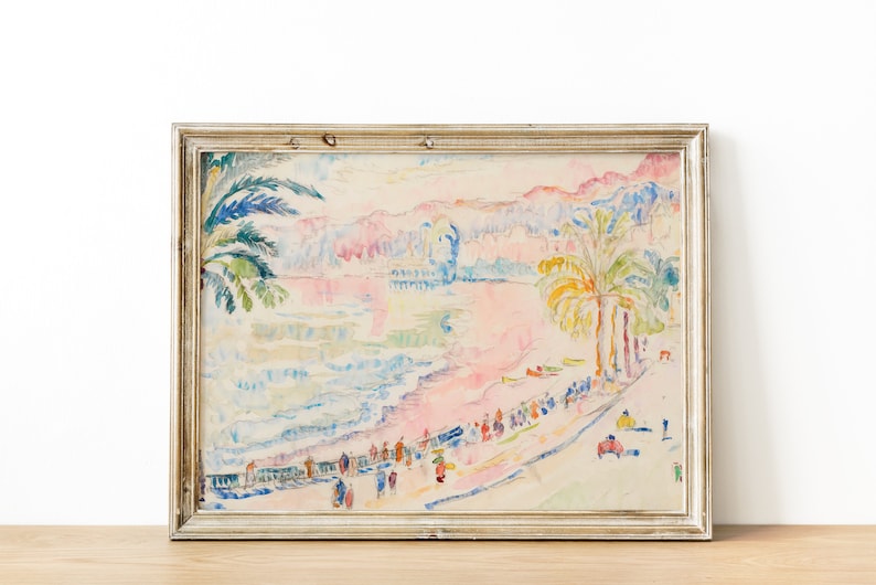 May include: A framed watercolor painting of a beach scene with palm trees, figures, and buildings. The artwork features pastel colors, including pink, blue, and yellow. The frame is a light, neutral color.