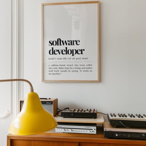 May include: A framed print with a black and white definition of a software developer. The definition reads: "[sohf-t-wair dih-vel-uh-per] noun a caffeine-fueled wizard who turns coffee into code, fights bugs for a living, and makes stuff work-usually by saying, "It works on my machine.""