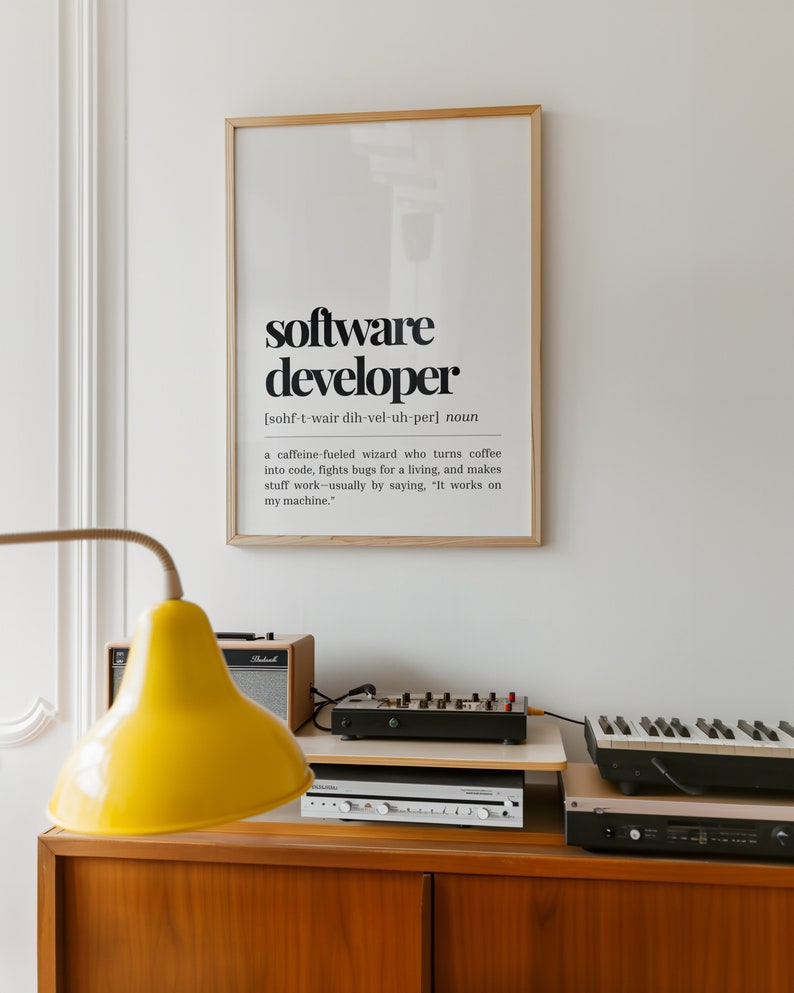 May include: A framed print with a black and white definition of a software developer. The definition reads: "[sohf-t-wair dih-vel-uh-per] noun a caffeine-fueled wizard who turns coffee into code, fights bugs for a living, and makes stuff work-usually by saying, "It works on my machine.""