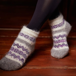 May include: A pair of white wool socks with a purple and gray geometric pattern. The socks are worn on a person's feet.