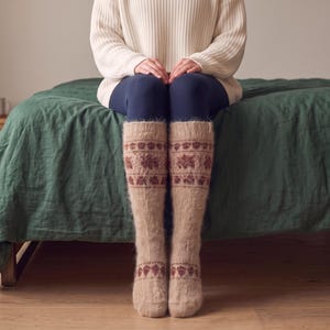 May include: A pair of knee-high beige fuzzy socks featuring a repeating dark brown floral and leaf pattern around the calf and a smaller matching band of patterns near the ankle, crafted from a soft, textured knit material with a visible fiber pile.