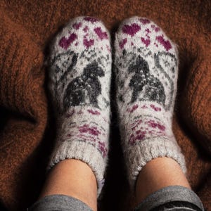 May include: A pair of white wool socks with a pink and black pattern. The socks feature a small animal design.