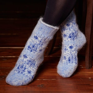 Könnte beinhalten: Ein Paar blaue und weiße Stricksocken mit einem Schneeflockenmuster. Die Socken sind aus weichem, flauschigem Garn.