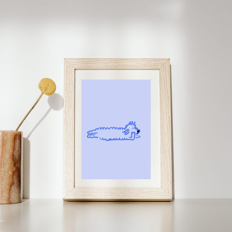 May include: A framed art print featuring a light blue background with a blue illustration of a dog lying down. The dog is drawn in a minimalist style. The frame is made of light-colored wood.