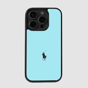 Puede incluir: Una funda de teléfono con fondo azul claro y borde negro. La funda presenta un logotipo de jugador de polo negro. La funda del teléfono tiene un módulo de cámara con tres lentes.