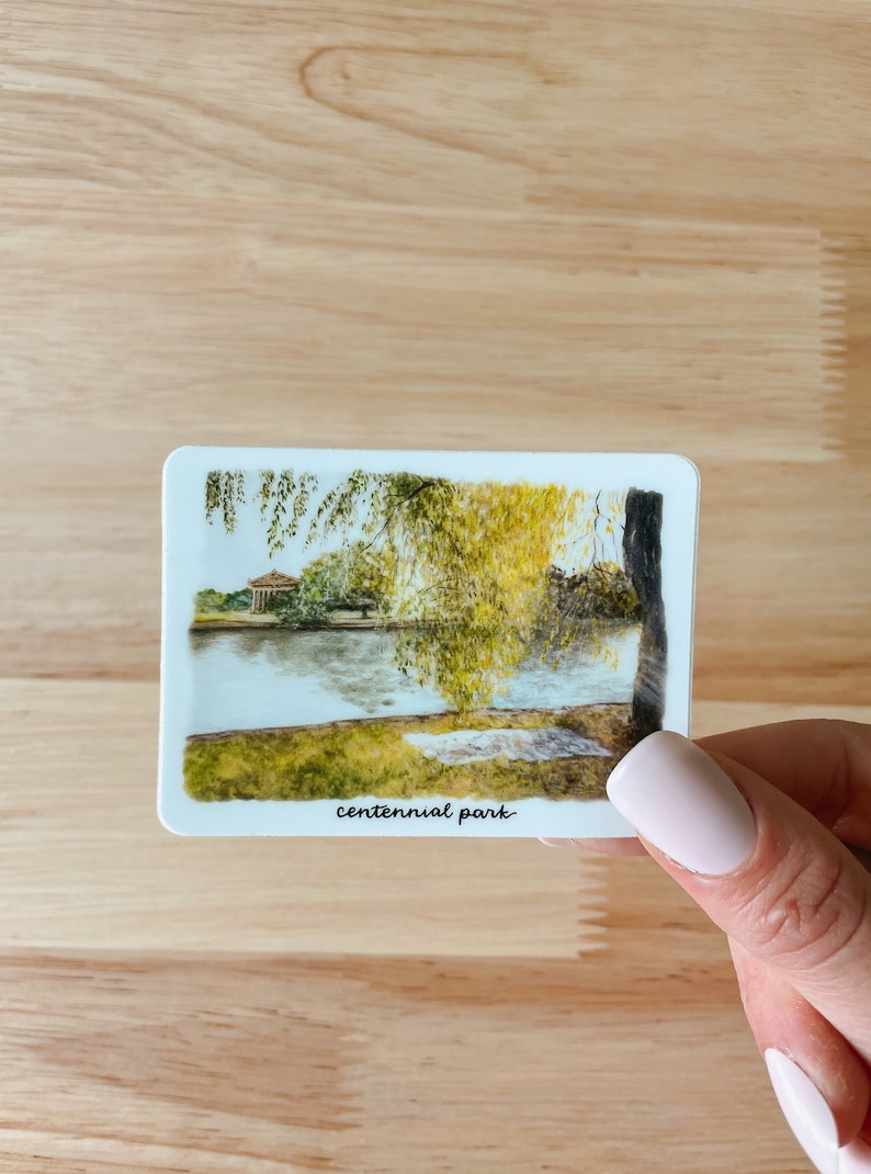Pu&ograve; includere: Un'illustrazione ad acquerello di una scena di parco con un lago, alberi e un piccolo edificio in lontananza. Il testo "centennial park" &egrave; scritto in basso nell'immagine.