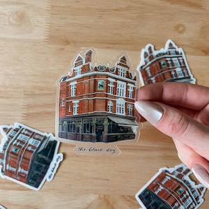 May include: A clear sticker with a watercolor illustration of a red brick building with a sign that reads "The Black Dog".