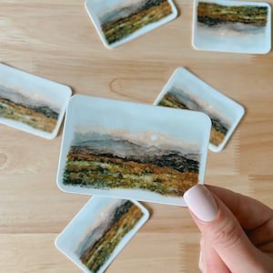 May include: A set of five watercolor landscape stickers featuring a sunset over a mountain range. The stickers are printed on white paper and have a matte finish. The stickers are approximately 2 inches by 3 inches in size. #stickers #watercolor #landscape #sunset #mountain #nature #art #handmade #smallbusiness
