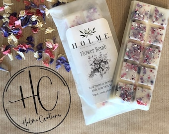 Könnte beinhalten: Ein weißer Wachsschmelzblock mit rosa und violetten Sprenkeln. Der Block ist mit "HOLME Flower Bomb" beschriftet und trägt den Hinweis "Hand Poured in Hertford, Made from 100% Soy, Vegan - Cruelty Free".