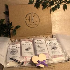 May include: A gift box filled with five small wax melts, each with a different scent and design. The scents are Love Spells, Pomegranate Nolt, Lavender Breeze, and Flower Bomb. The box is decorated with a small wooden heart.