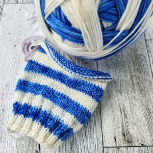 May include: A blue and white striped knitted fabric with a ball of blue and white yarn in the background.