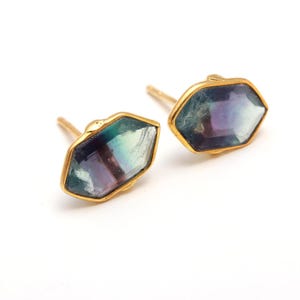 Può includere: Un paio di orecchini dorati con una pietra geometrica, sfaccettata, iridescente verde, blu e viola.