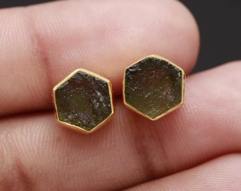 Op de afbeelding: Een paar gouden oorbellen met zeshoekige groene edelsteen bezettingen.