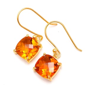 May include: A pair of gold earrings with orange gemstone drops. The earrings have a simple, elegant design.