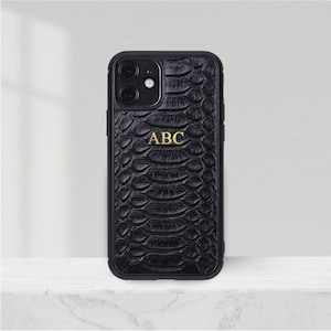Może przedstawiać: Czarne etui na telefon z wzorem skóry węża i złotym napisem "ABC".