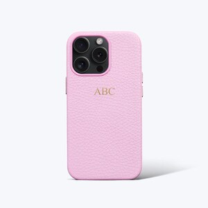 May include: A pink leather phone case with a monogram of the letters "ABC" in gold. The case has a textured surface and is designed for an iPhone.
