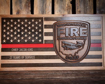 May include: A wooden American flag with a red stripe, a black and white star pattern, and a brown woodgrain background. The flag has the text "Wright-Patterson AFB Fire Emergency Services" and "USAF" on it. The flag also has the text "Chief Jacob King 27 Years of Service" on it.