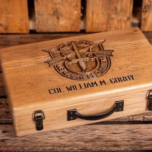 May include: A wooden box with a carved military insignia and the name "COL WILLIAM M. GORBY" engraved on the front. The box has a black handle and two metal clasps.