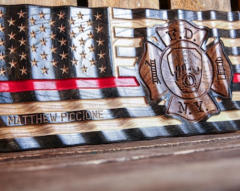 Puede incluir: Una bandera americana de madera con una franja roja y una insignia de bombero en el centro. La insignia es una cruz con una boca de incendios en el centro y las letras "F.D. N.Y.". La bandera está personalizada con el nombre "MATTHEW PICCIONE".