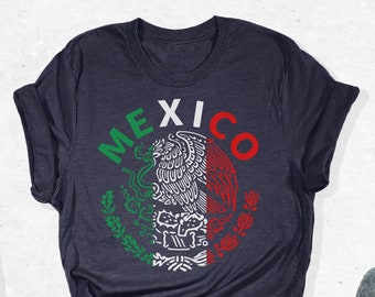May include: A navy blue t-shirt with a white graphic of the Mexican coat of arms and the word "MEXICO" in white lettering. The shirt is folded and laid flat on a white surface.