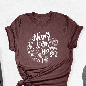 May include: A maroon t-shirt with a white graphic that says "Never Grow Up" and features various Disney icons.