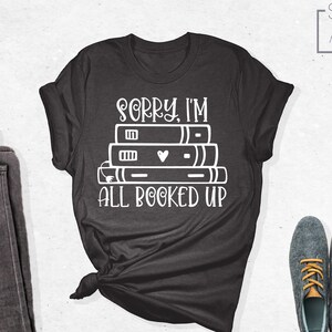 May include: A dark gray t-shirt with the text "Sorry, I'm all booked up" and a stack of books with a heart on the top book.