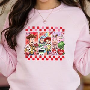 A woman wearing a pink sweatshirt with a graphic of characters from the Toy Story movie.
