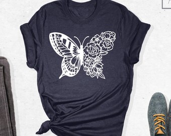 May include: A navy blue t-shirt with a white butterfly design featuring floral details. The butterfly is centered on the shirt and has a delicate, intricate design.