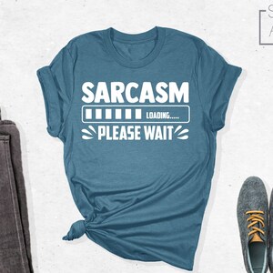 May include: A teal blue t-shirt with the text "SARCASM LOADING... PLEASE WAIT" in white.