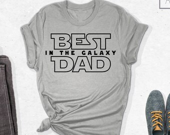 May include: A gray t-shirt with the text "BEST IN THE GALAXY DAD" in black lettering. The shirt is folded and laid flat on a white surface.